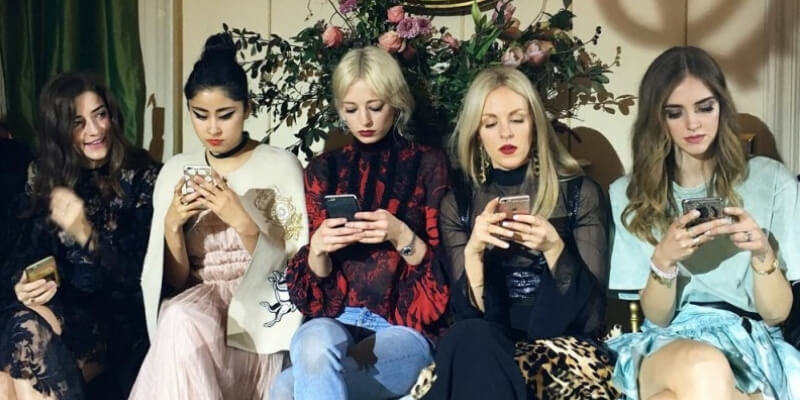 delle influencer guardano il telefono durante una sfilata