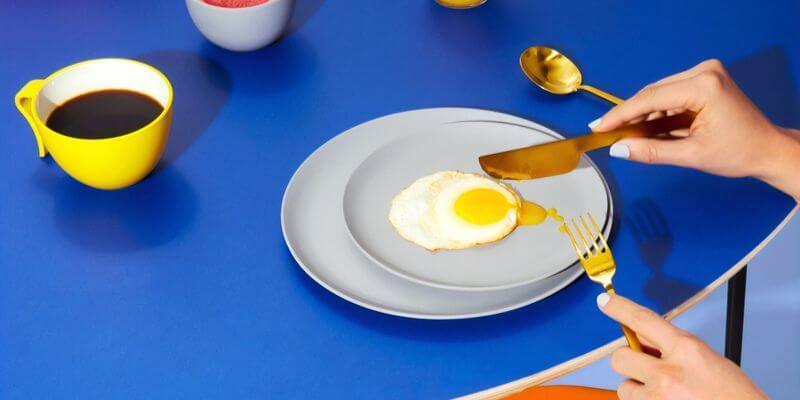 close up di un piatto con uovo fritto su tavolo blu