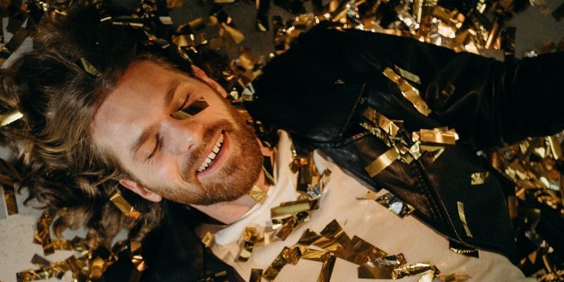 Un ragazzo sdraiato sul pavimento con addosso dei confetti color oro