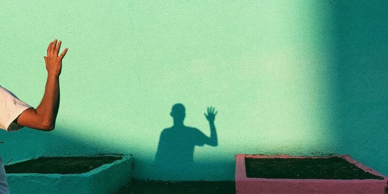 un ragazzo con il braccio alzato in saluto proietta la sua ombra su un muro verde