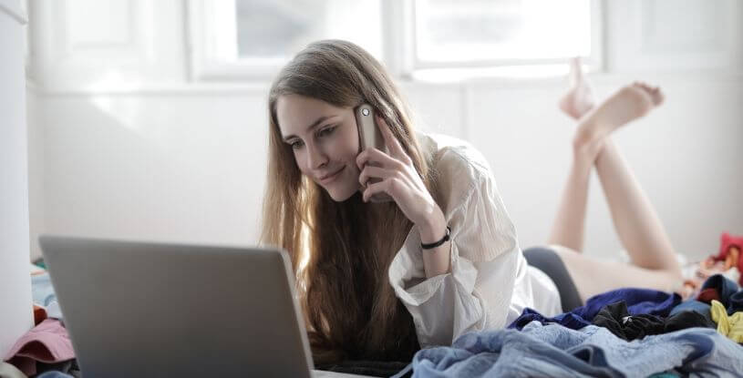 una ragazza sul letto con pc mentre sta al telefono