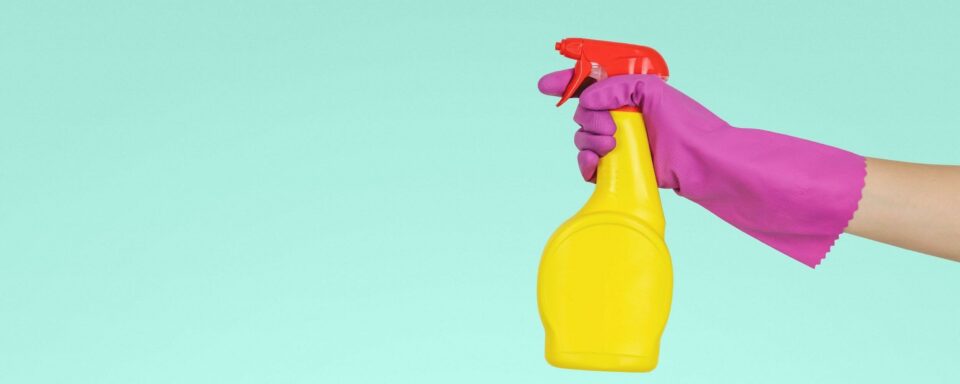 una mano con un guanto di gomma e un detersivo